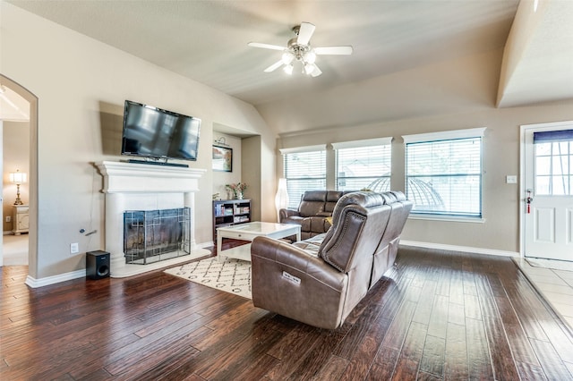 living area featuring baseboards, arched walkways, a fireplace with raised hearth, and wood finished floors