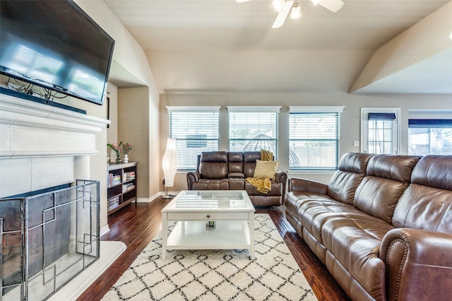 living area with a fireplace with raised hearth, lofted ceiling, a ceiling fan, baseboards, and dark wood-style floors