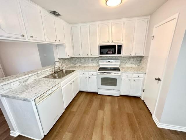 kitchen with white appliances, visible vents, white cabinets, light countertops, and a sink