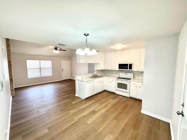 kitchen with white electric stove, light countertops, stainless steel microwave, white cabinets, and a sink