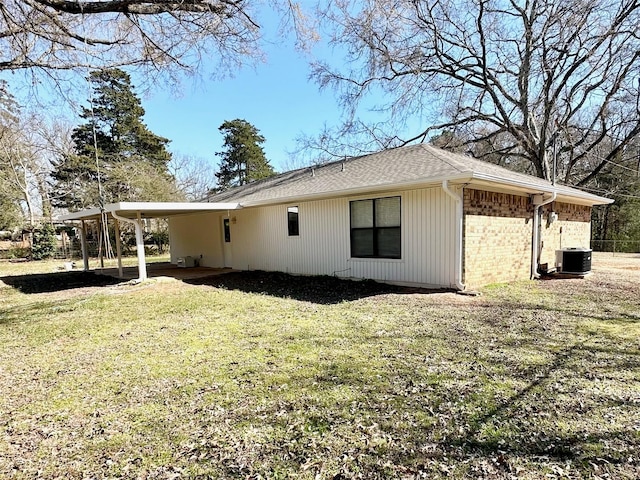 view of side of home featuring brick siding, a yard, central air condition unit, a shingled roof, and an attached carport