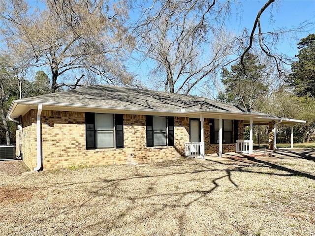 view of front of property with a shingled roof, cooling unit, covered porch, and brick siding