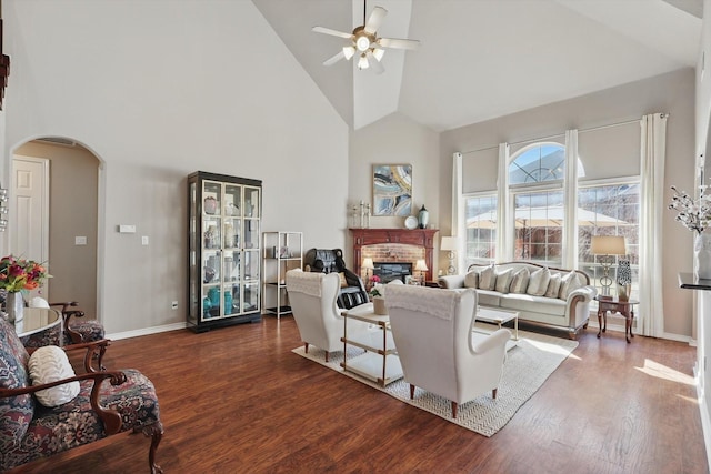 living room featuring a ceiling fan, arched walkways, dark wood-type flooring, and a glass covered fireplace