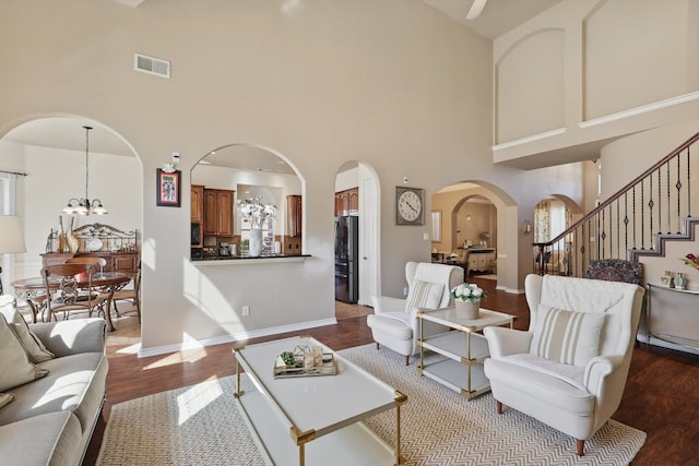 living area with arched walkways, a chandelier, wood finished floors, visible vents, and stairs