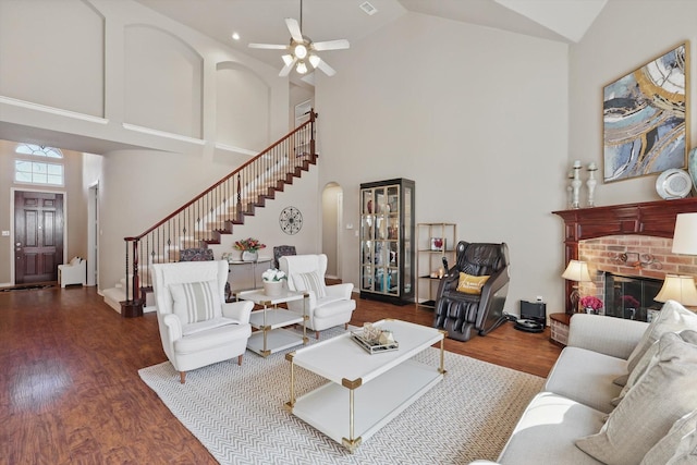 living room featuring high vaulted ceiling, a brick fireplace, stairway, and wood finished floors