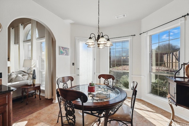 dining space featuring light tile patterned floors, baseboards, visible vents, and arched walkways