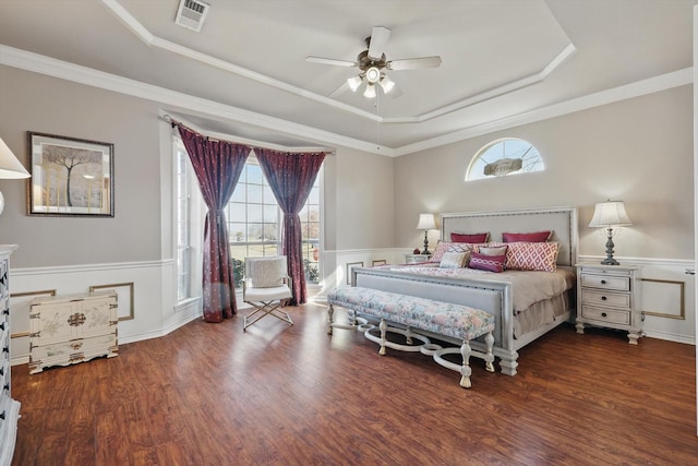 bedroom with a wainscoted wall, a tray ceiling, multiple windows, and visible vents