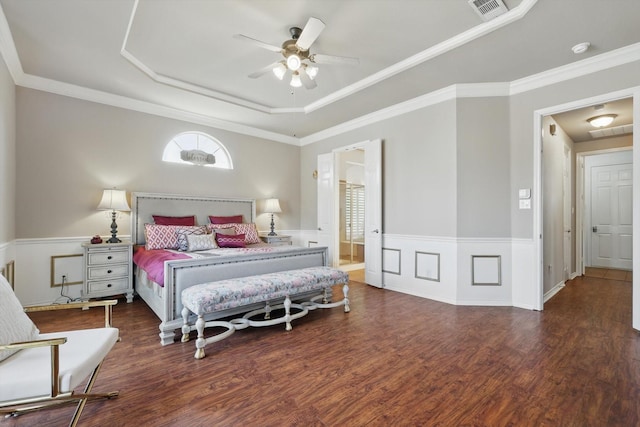 bedroom featuring a wainscoted wall, crown molding, a raised ceiling, and wood finished floors