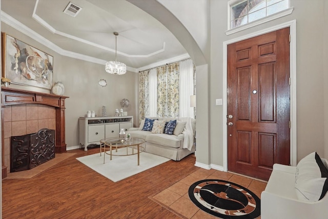 foyer entrance featuring arched walkways, crown molding, a fireplace, a raised ceiling, and visible vents