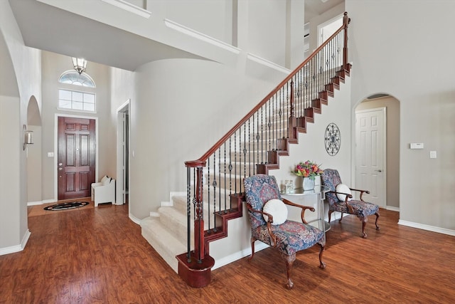 entryway featuring arched walkways, wood finished floors, a towering ceiling, and baseboards