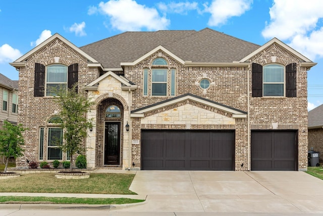 french country inspired facade with an attached garage, a shingled roof, concrete driveway, and brick siding