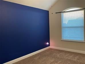 carpeted empty room with baseboards and vaulted ceiling