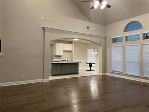 unfurnished living room with arched walkways, ceiling fan, wood finished floors, high vaulted ceiling, and baseboards