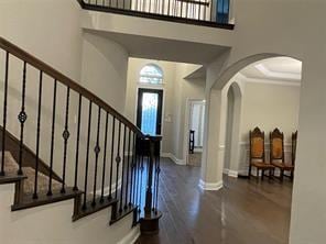 foyer entrance featuring arched walkways, stairway, a high ceiling, wood finished floors, and baseboards