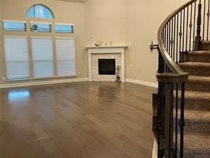 unfurnished living room with baseboards, a fireplace, stairway, and wood finished floors