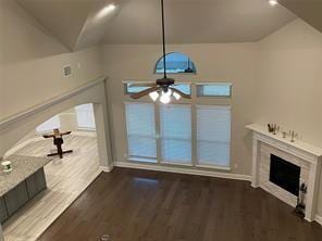 unfurnished living room featuring ceiling fan, a fireplace, vaulted ceiling, and wood finished floors