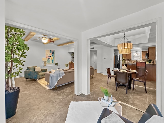 living room with baseboards, a tray ceiling, and ceiling fan with notable chandelier