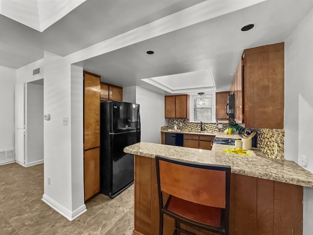 kitchen featuring brown cabinets, visible vents, backsplash, a peninsula, and black appliances