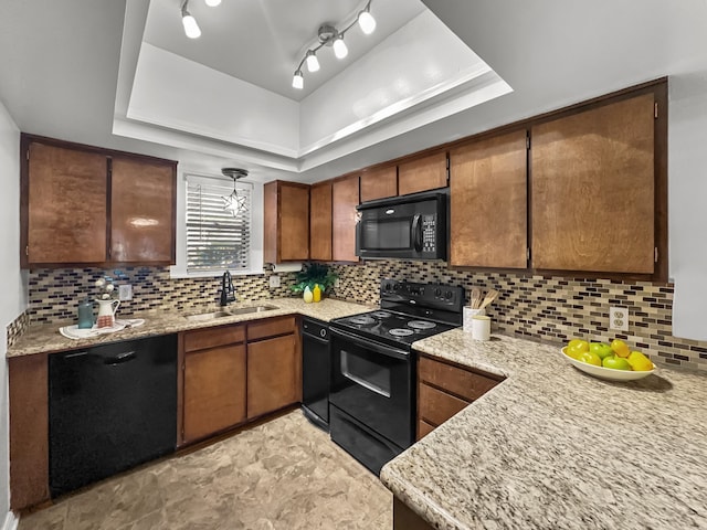 kitchen with tasteful backsplash, light stone counters, a tray ceiling, black appliances, and a sink