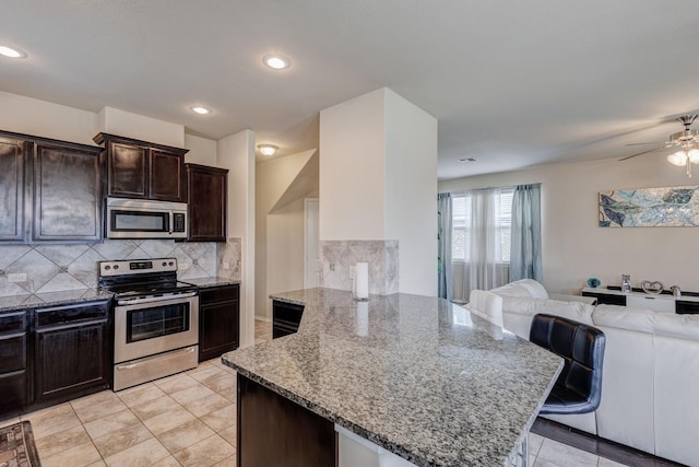 kitchen featuring light stone countertops, stainless steel appliances, dark brown cabinets, open floor plan, and backsplash