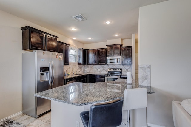 kitchen with visible vents, dark brown cabinetry, light stone counters, decorative backsplash, and stainless steel appliances