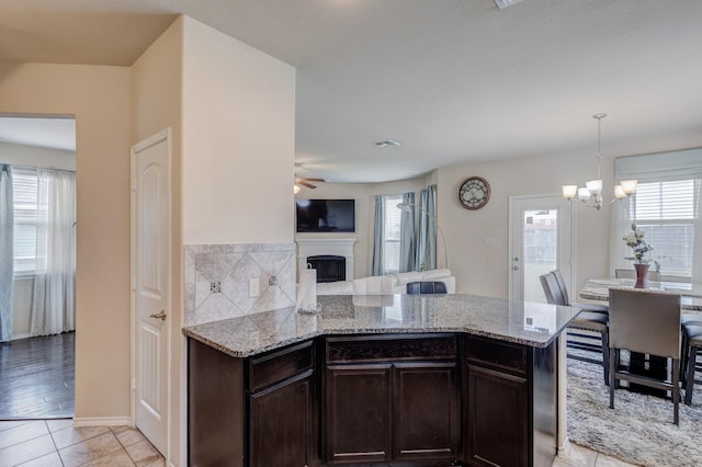 kitchen with light stone counters, dark brown cabinetry, a peninsula, a fireplace, and light tile patterned floors