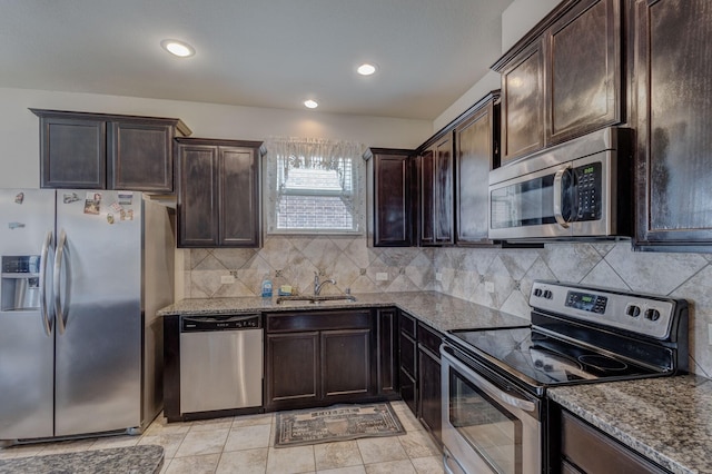 kitchen featuring dark stone countertops, dark brown cabinetry, appliances with stainless steel finishes, and a sink