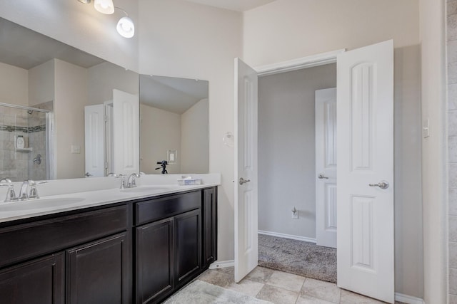 bathroom with double vanity, a shower stall, baseboards, and a sink