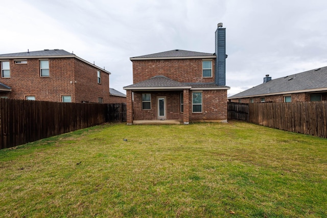 back of property with a lawn, brick siding, a fenced backyard, and a chimney