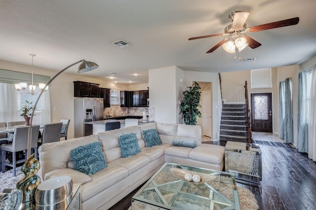 living area with visible vents, ceiling fan with notable chandelier, dark wood finished floors, and stairway