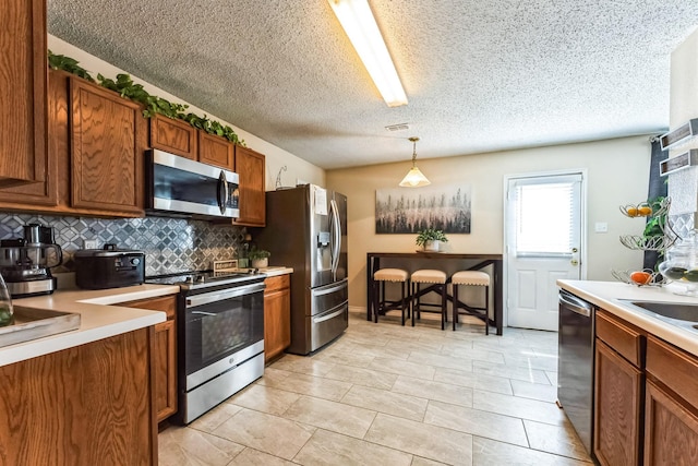 kitchen with brown cabinets, stainless steel appliances, visible vents, light countertops, and backsplash