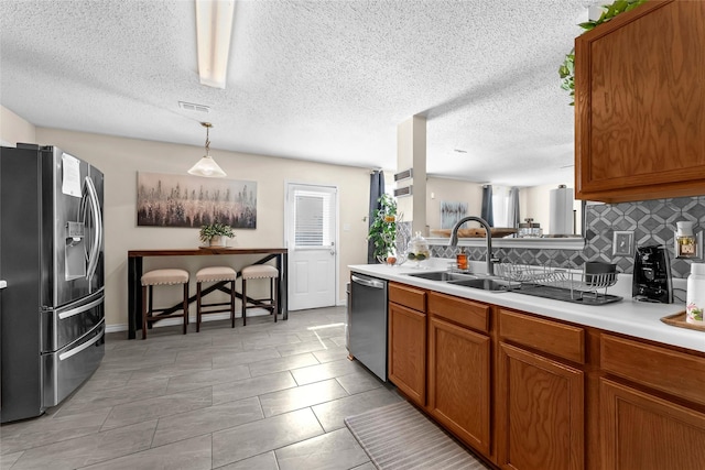 kitchen featuring stainless steel appliances, light countertops, visible vents, brown cabinetry, and a sink