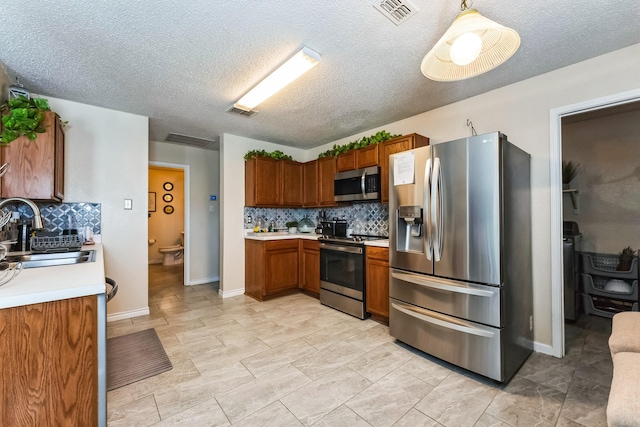 kitchen featuring brown cabinets, light countertops, visible vents, appliances with stainless steel finishes, and a sink