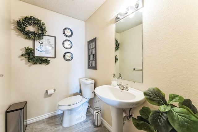 half bathroom featuring toilet, a sink, baseboards, and a textured ceiling