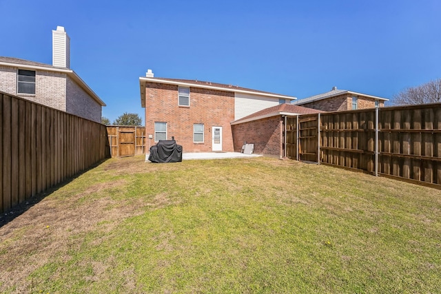 rear view of house with a fenced backyard, a gate, a yard, a patio area, and brick siding