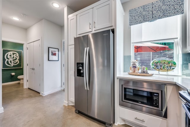 kitchen featuring appliances with stainless steel finishes, backsplash, finished concrete flooring, and baseboards