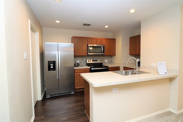 kitchen with stainless steel appliances, a peninsula, a sink, tasteful backsplash, and brown cabinetry