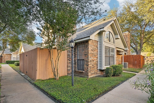 view of side of property featuring brick siding, a shingled roof, and fence