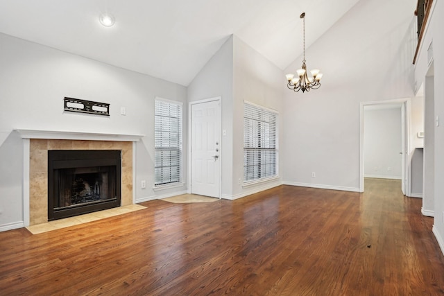 unfurnished living room with high vaulted ceiling, wood finished floors, baseboards, a tiled fireplace, and an inviting chandelier