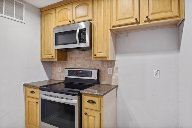 kitchen featuring dark stone countertops, visible vents, stainless steel appliances, and backsplash