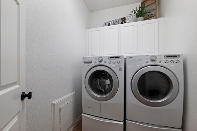 washroom featuring a textured wall, washing machine and dryer, and cabinet space