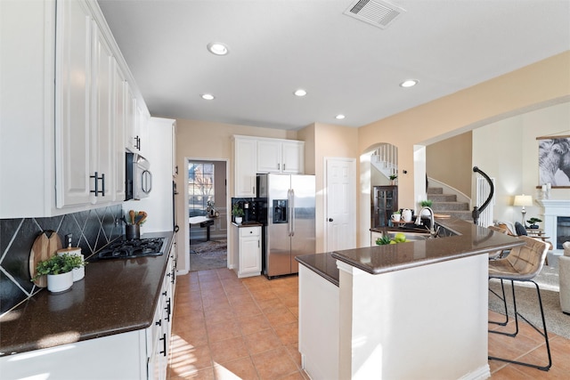 kitchen with stainless steel appliances, visible vents, a kitchen breakfast bar, decorative backsplash, and dark countertops