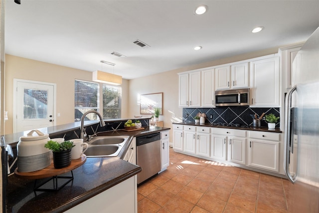 kitchen with dark countertops, visible vents, backsplash, appliances with stainless steel finishes, and a sink