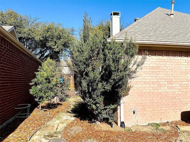 view of property exterior featuring brick siding, roof with shingles, and a chimney