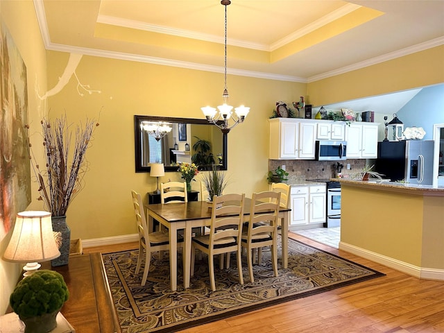 dining area featuring light wood finished floors, baseboards, a tray ceiling, and a chandelier