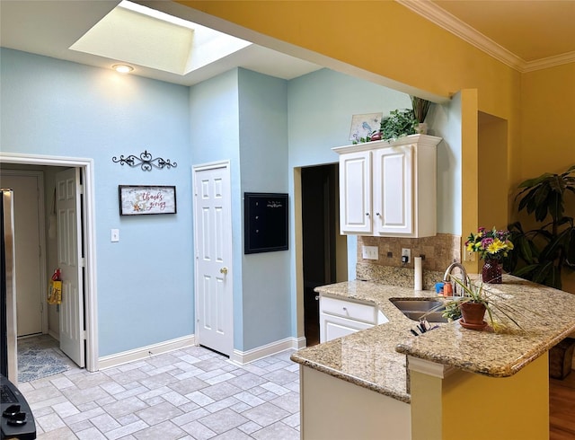 kitchen with a peninsula, a skylight, a sink, baseboards, and tasteful backsplash