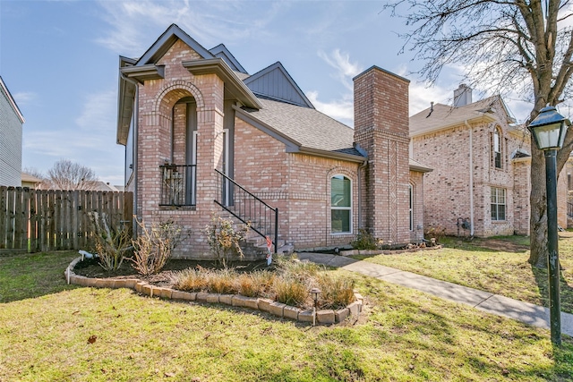 view of front of house with a front lawn, a shingled roof, fence, and brick siding