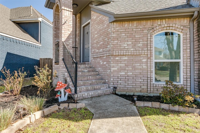 property entrance featuring roof with shingles and brick siding