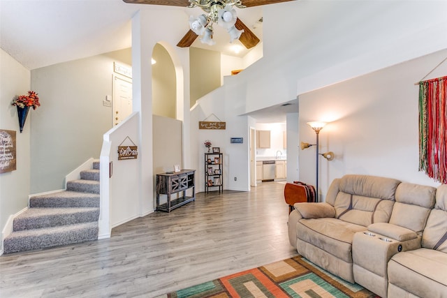 living area featuring baseboards, ceiling fan, stairway, light wood-style floors, and high vaulted ceiling