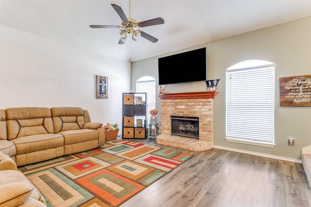 living area with ceiling fan, a textured ceiling, wood finished floors, baseboards, and a brick fireplace